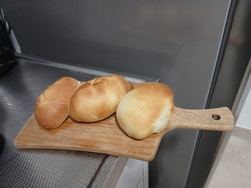 Três pães de leite pequenos em cima de uma tábua de madeira